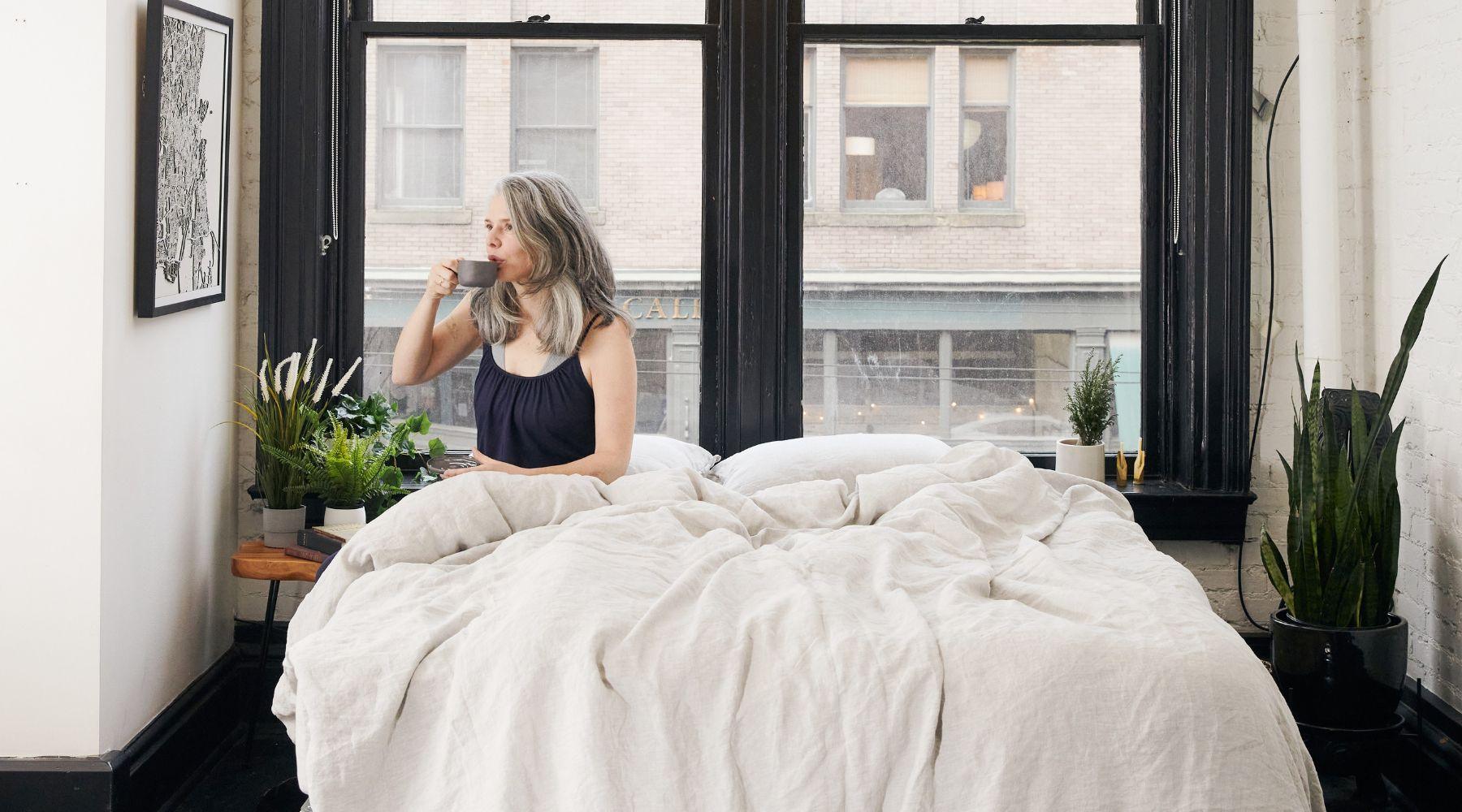 Woman drinking a cup of tea on bed made with organic European linen bedding by The Modern Dane